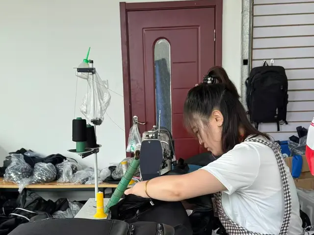 Operator reinforcing a backpack strap anchor on a bartack machine